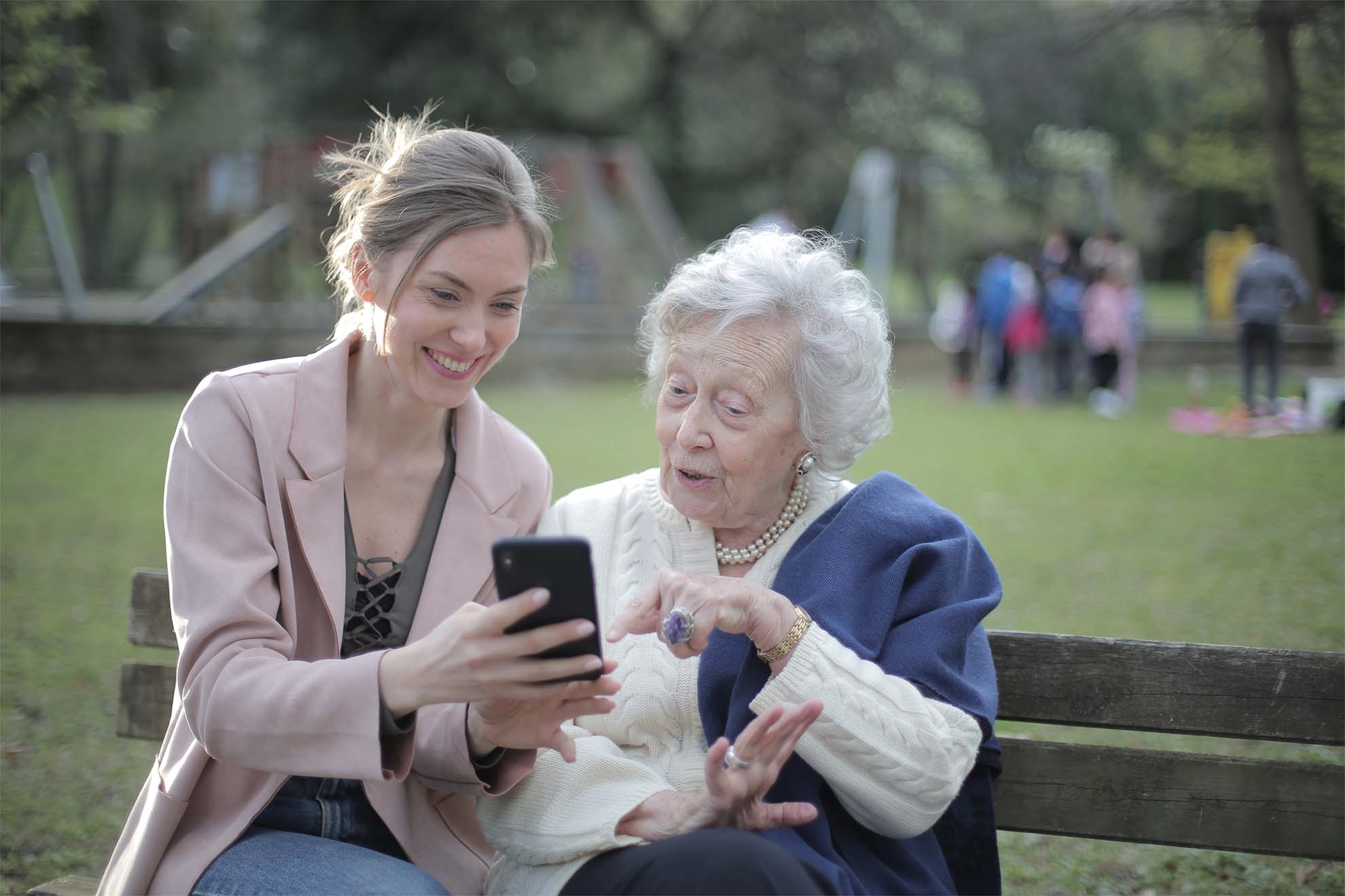 resident and loved one in a park sat on a bench looking at a phone